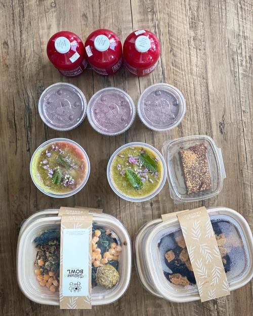 A variety of colorful food containers and drinks arranged on a wooden surface, featuring salads, desserts, and beverages.