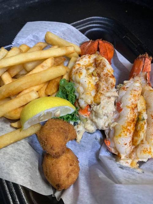 A plate featuring lobster tails, fried shrimp, French fries, a lemon wedge, and two hushpuppies on a bed of lettuce.