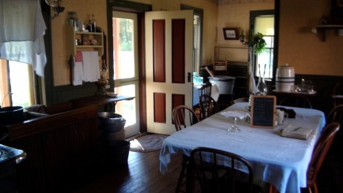 A cozy dining room with a white tablecloth, wooden chairs, and a door leading to a sunny outdoor area.