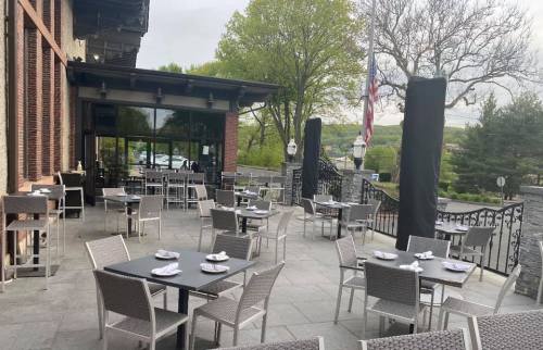 Outdoor dining area with empty tables and chairs, surrounded by greenery and a view of the landscape.