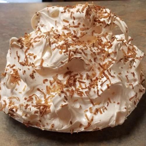 A fluffy meringue pie topped with toasted coconut flakes on a rustic countertop.