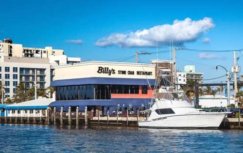 A waterfront restaurant named Billy's Stone Crab, with a boat docked nearby and a clear blue sky above.