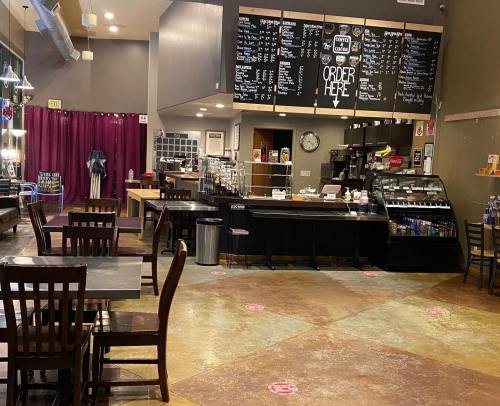 Interior of a coffee shop with wooden tables, a counter displaying a menu, and a cozy atmosphere.