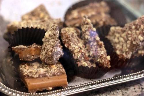 A tray of assorted chocolate treats, including nut-covered pieces and caramel squares, arranged in black liners.