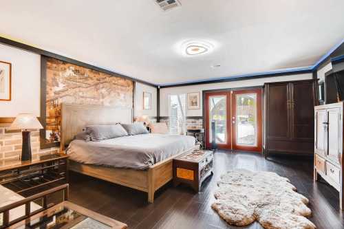 Cozy bedroom featuring a large bed, wooden furniture, decorative wall art, and natural light from double doors.