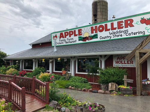 A rustic building with a sign reading "Apple Holler" featuring a farm, restaurant, and wedding venue, surrounded by greenery.