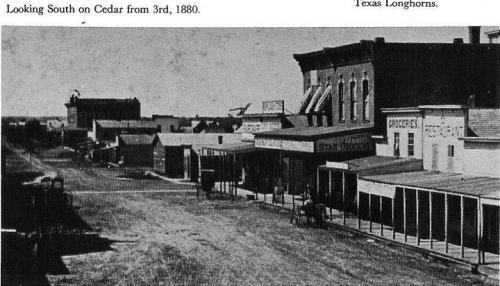 Historic black-and-white photo of a street scene in 1880, showing storefronts and a clear sky.