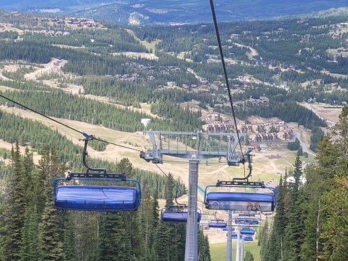 A scenic view from a ski lift, overlooking green mountains and a valley with buildings below.