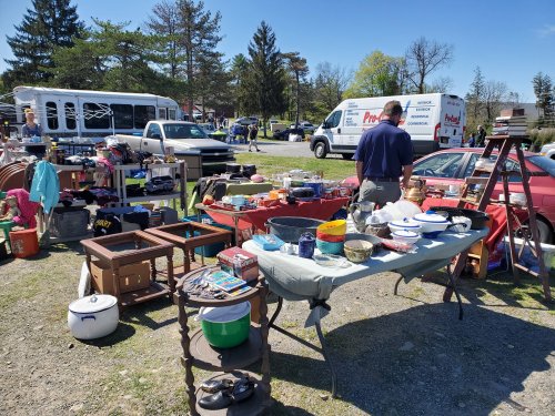 A bustling flea market scene with tables of various items for sale and a person browsing among the goods.