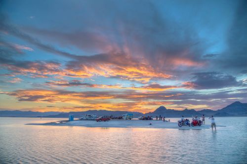 A scenic sunset over a salt flat, with vehicles and people enjoying the view against a colorful sky.