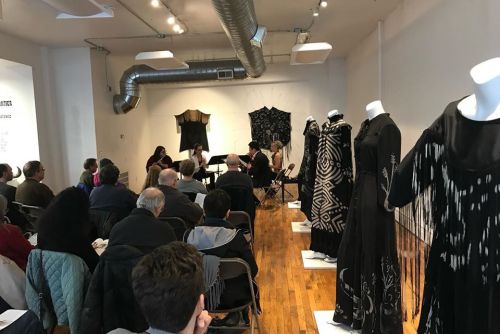 A panel discussion in a gallery, with attendees seated and black garments displayed on mannequins.