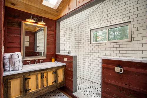 A rustic bathroom featuring a wooden vanity, white subway tile, and a skylight for natural light.