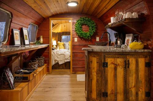 Cozy interior of a rustic cabin with wooden walls, a kitchenette, and a warm, inviting bedroom in the background.