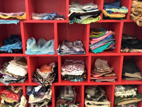 A colorful display of neatly folded fabrics in various patterns and textures, organized on red shelves.