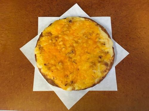 A round, cheesy pizza with a golden-brown crust, placed on a white paper square on a wooden surface.