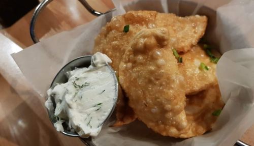 A basket of golden fried dumplings served with a side of creamy herb dip.