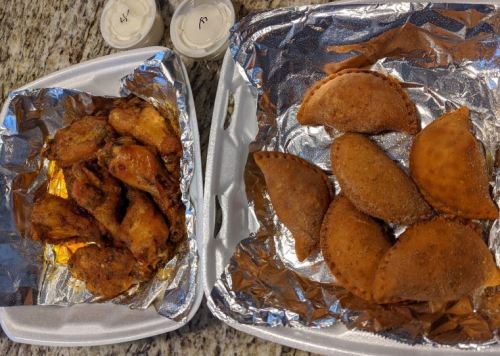 Two trays of food: one with crispy chicken wings and the other with golden-brown empanadas, accompanied by dipping sauces.