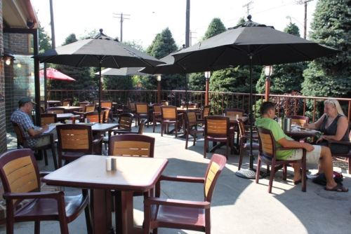 Outdoor dining area with tables and umbrellas, featuring patrons enjoying their meals in a shaded setting.