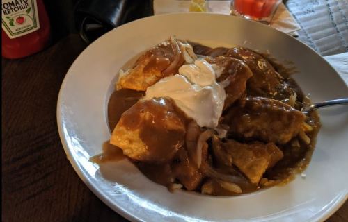 A plate of enchiladas topped with sour cream and a rich brown sauce, served with onions.
