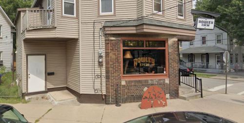 Exterior view of Rowley Inn, a corner building with a sign, large windows, and a small outdoor area.