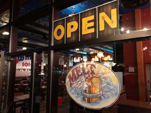 A brightly lit restaurant entrance with an "OPEN" sign and a colorful "MELT" logo on the window.