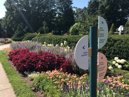 A vibrant garden path with colorful flowers and directional signs for various garden areas.