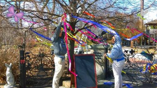 Two people decorate a tree with colorful ribbons at Hershey Children's Garden, surrounded by playful decorations.