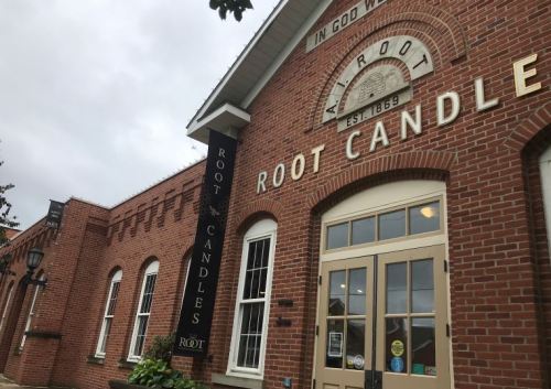 Exterior of the Root Candle building, featuring brick walls, large windows, and a sign with the company name.