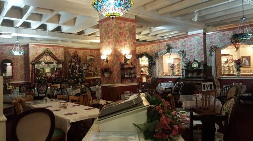 Cozy restaurant interior with floral wallpaper, vintage decor, and tables set for dining under colorful stained glass lights.
