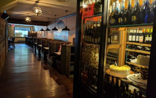 A cozy restaurant interior featuring a long hallway, wine display, and tables with booths along the walls.