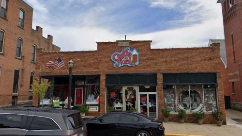 A brick storefront with a colorful sign reading "The Snack," featuring large windows and decorative plants outside.