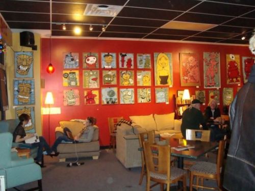 A cozy café with colorful artwork on the walls, featuring people relaxing and socializing in a warm atmosphere.