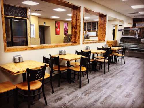 A cozy restaurant interior with wooden tables, chairs, and a large mirror reflecting the space.