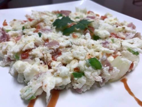 A plate of scrambled eggs mixed with diced tomatoes, green peppers, and ham, garnished with cilantro.