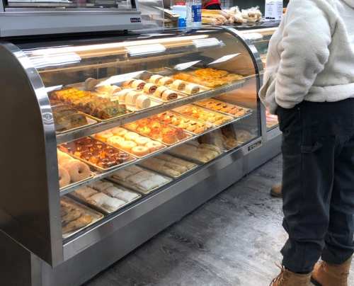 A display case filled with various baked goods, including pastries and donuts, with a person standing nearby.