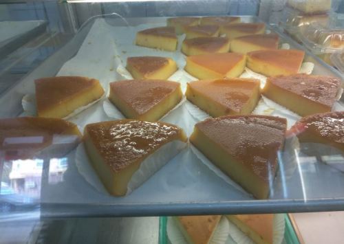 Slices of caramel flan arranged neatly on a tray, showcasing a glossy top and creamy yellow interior.