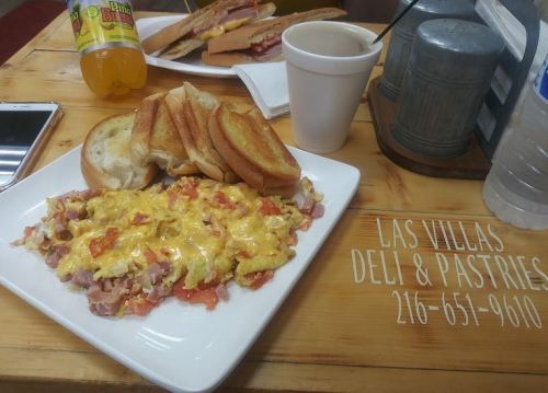 A plate of cheesy scrambled eggs with ham and tomatoes, served with toasted bread and a cup of coffee.