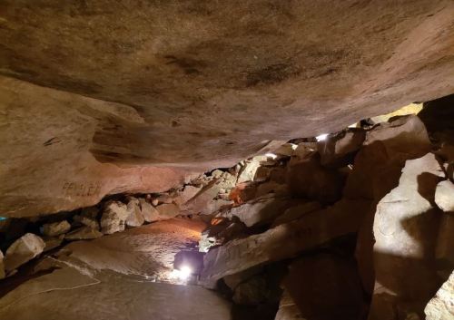 Dimly lit cave interior with rocky walls and scattered boulders, illuminated by soft lights.