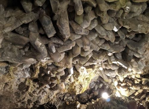 A cave ceiling covered with large, irregularly shaped rock formations, illuminated by a small light source.