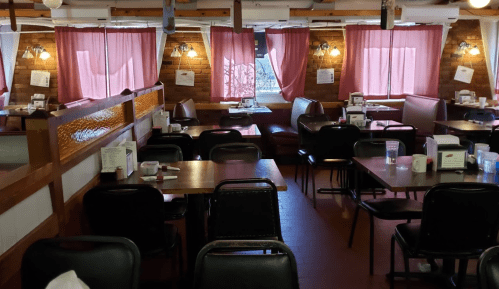Cozy restaurant interior with wooden tables, black chairs, and pink curtains, featuring a warm, inviting atmosphere.