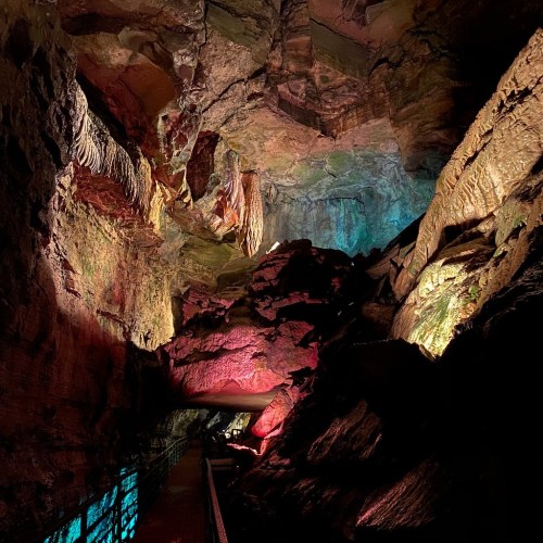 A colorful cave interior with illuminated rock formations and a pathway, showcasing natural textures and shadows.
