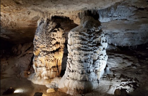 Stalactites and stalagmites in a dimly lit cave, showcasing intricate rock formations.