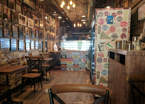 Cozy restaurant interior with wooden tables, framed photos on the walls, and a colorful fridge in the corner.