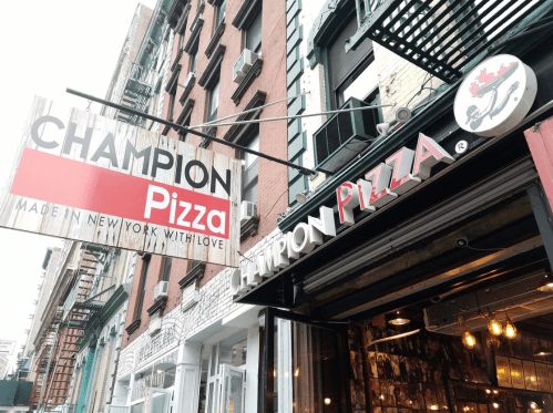 Signage for Champion Pizza in New York, featuring a red and white logo with "Made in New York with Love."