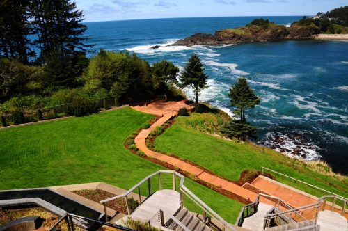 A scenic coastal view featuring a lush green lawn, winding pathways, and rocky shores under a blue sky.