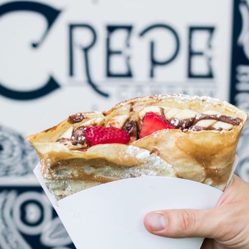 A hand holding a delicious crepe filled with chocolate, strawberries, and powdered sugar against a decorative background.