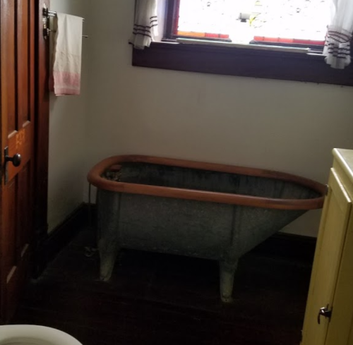 A vintage metal tub sits in a rustic bathroom with wooden walls and a window above it.
