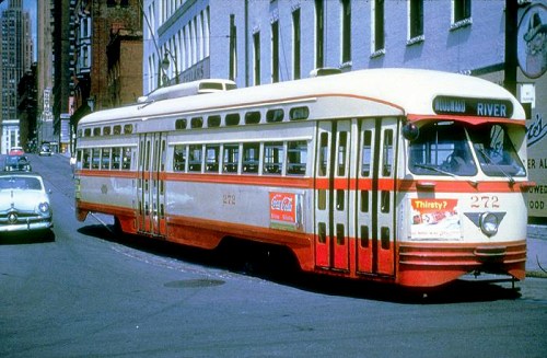 A vintage streetcar in red and cream colors, parked on a city street with buildings in the background.