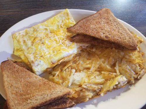 A plate with an omelette topped with cheese, crispy hash browns, and two slices of toasted bread.