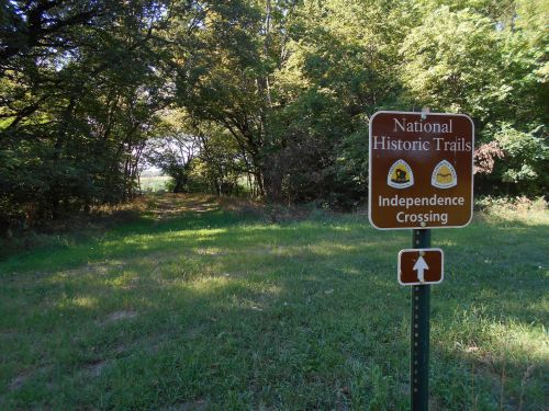 Sign for National Historic Trails at Independence Crossing, with a grassy path leading into a wooded area.